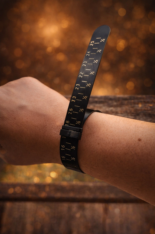Bracelet mesureur de taille de bague noir porté au poignet, graduations visibles de 16 à 25, photo ambiance luxe fond caramel — Étreinte Éternelle.